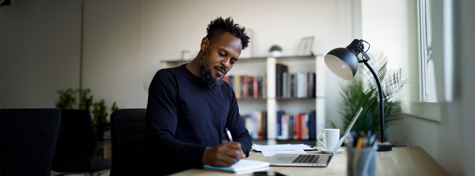 Man wearing a sweater is taking notes with a pen and paper