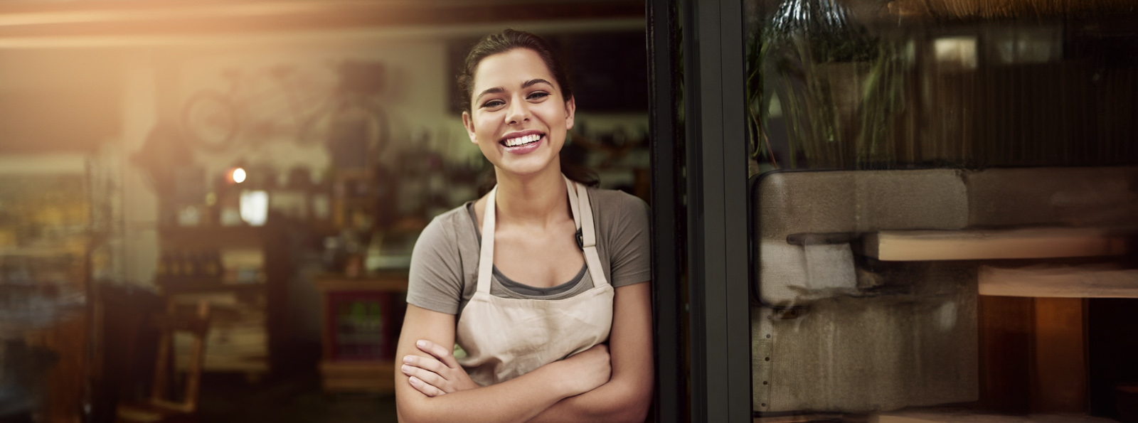 A female business owner stands by the door of her establishment and smiles at the camera