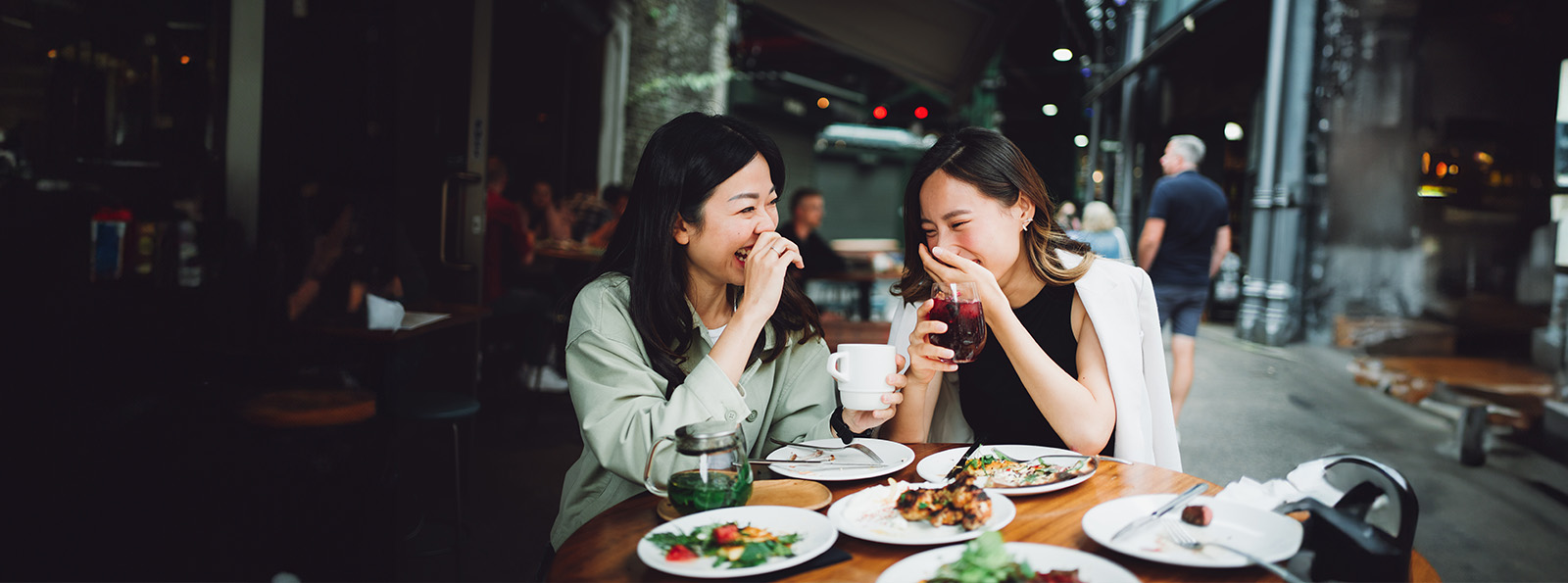 Two young women are seated in a restaurant and laughing while eating a meal