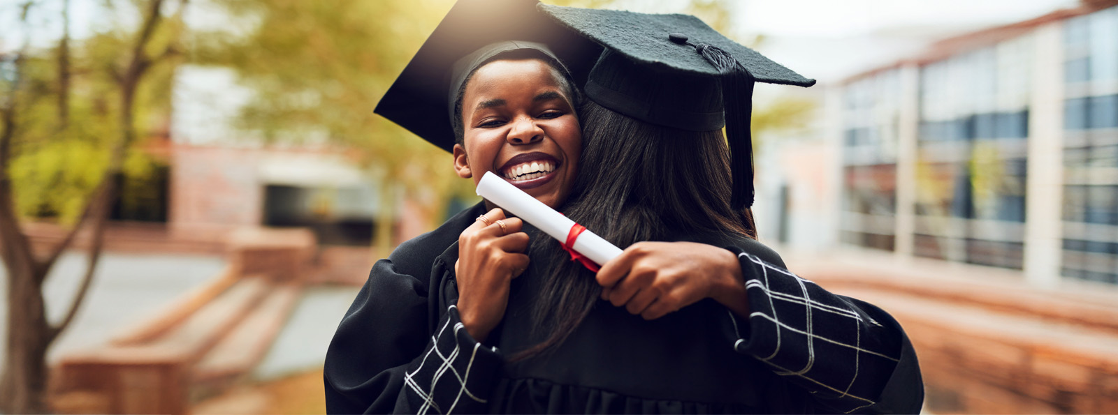 A young person dressed in cap and gown hugs his relative while holding his diploma