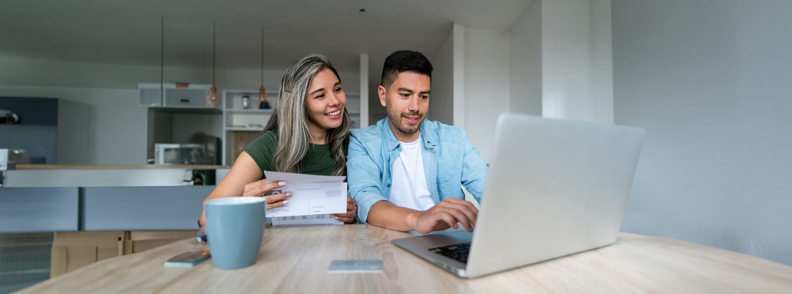 Woman and man are sitting at a kitchen table while looking at their laptop together