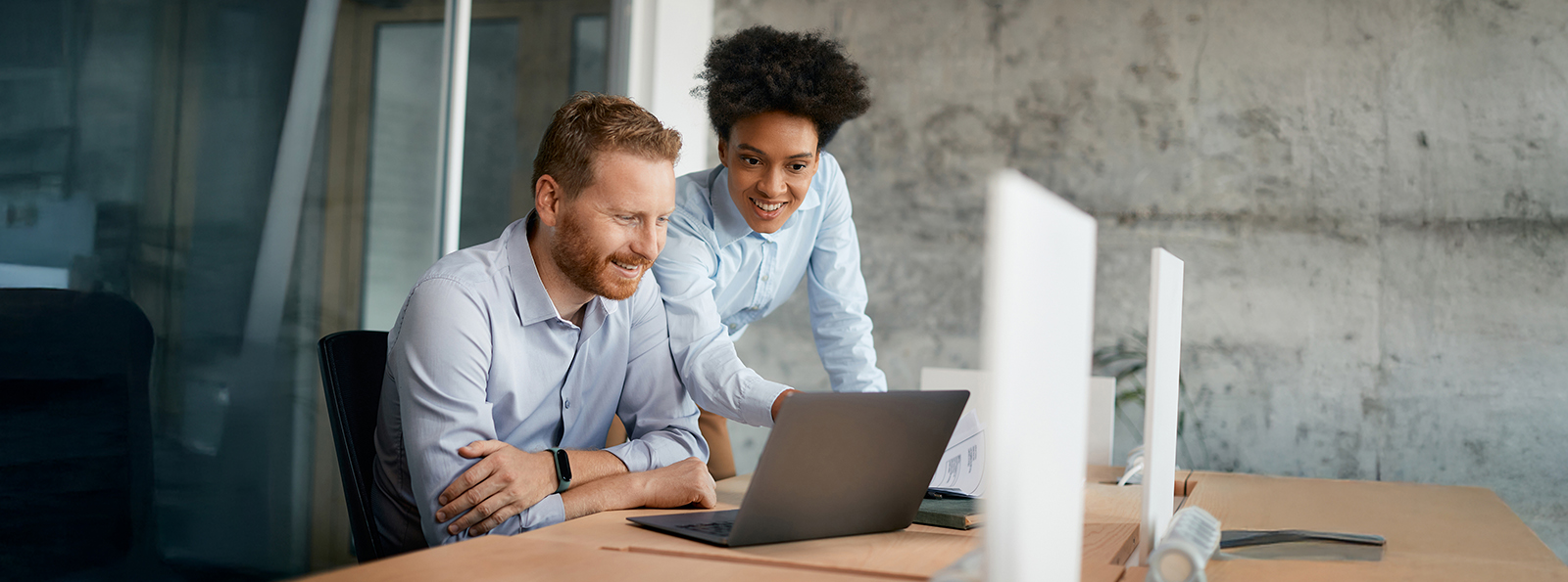 male and female co-workers review information on a laptop screen together