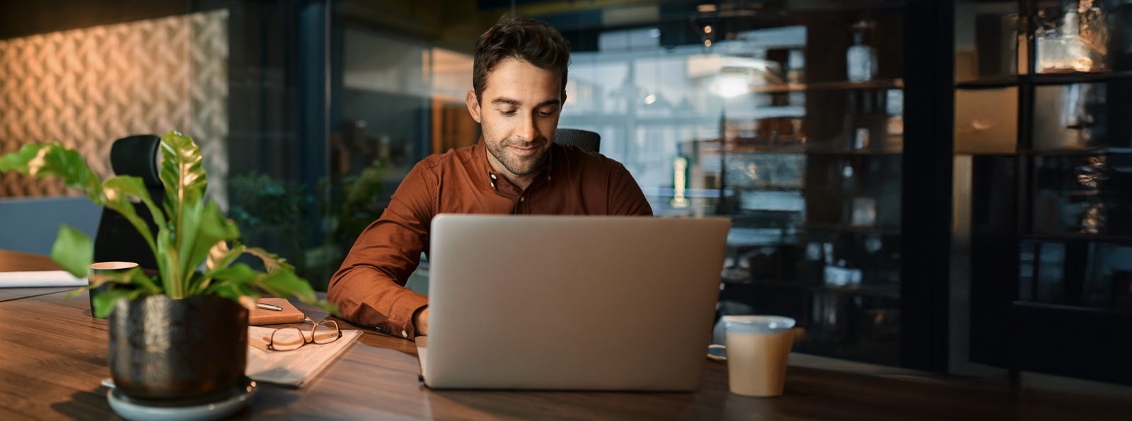 A young man has a soft smile as he works on his laptop