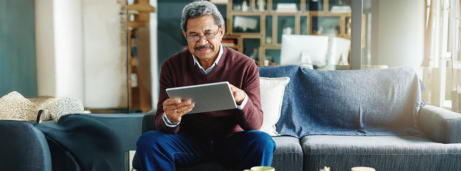 image of a mature man seated in his living room holding a smart tablet